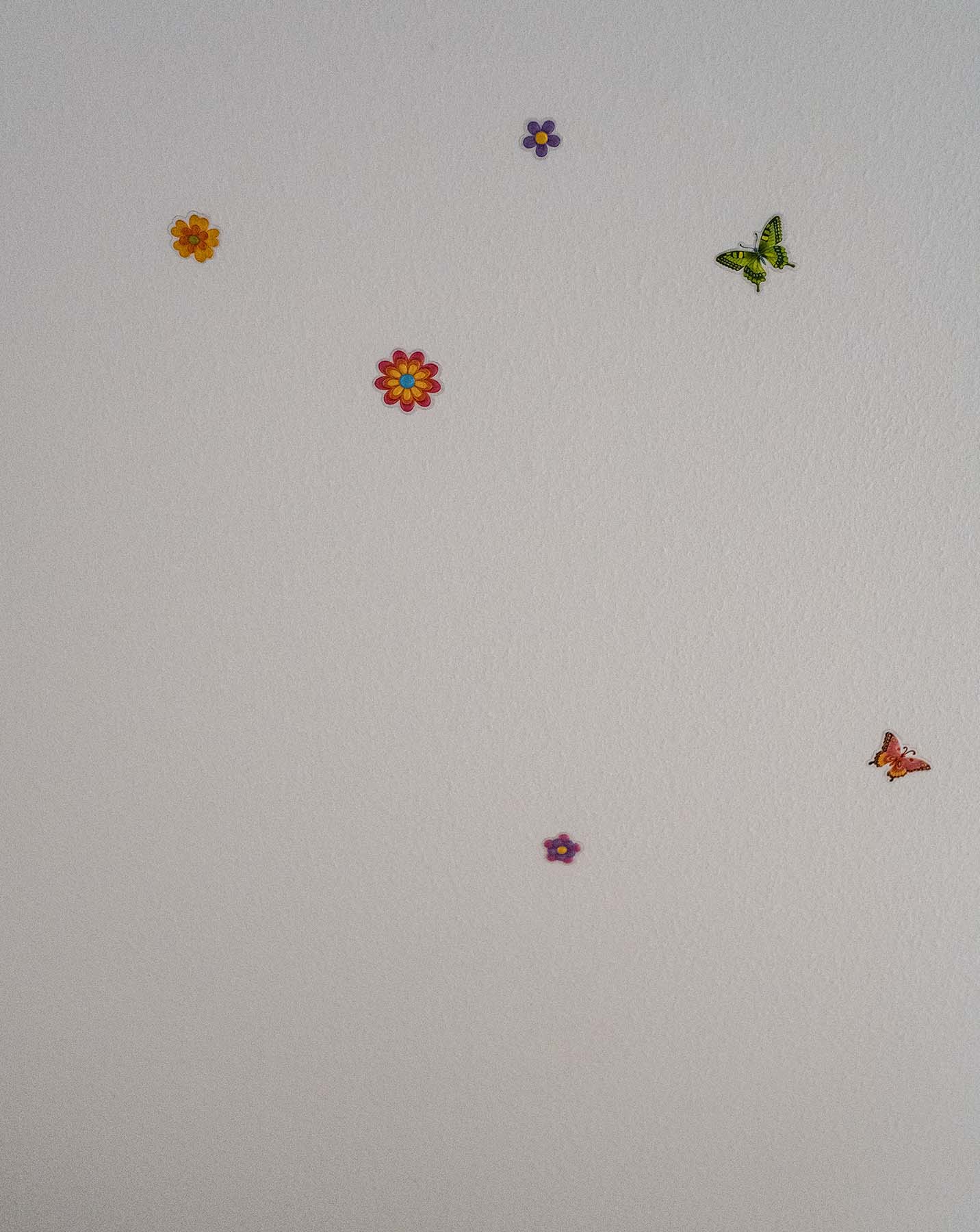 Ein wenig bunter Wandschmuck in Form von Blüten und Schmetterlingen. Gesprenkelt auf Rauhfasertapete.