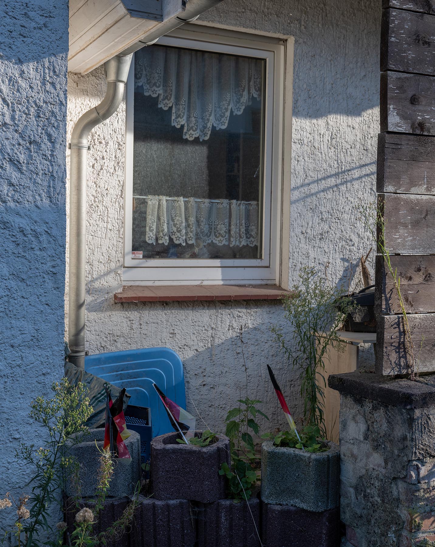 Blick auf ein Fenster im Erdgeschoss. Vier vergilbte Deutschlandfahnen stecken in Pflanzenkübeln
